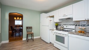 A kitchen with white cabinets, a stove, and a refrigerator. There is a dining area visible in the background. - Perfect Place and Breakfast Too! (Pittsburgh)
