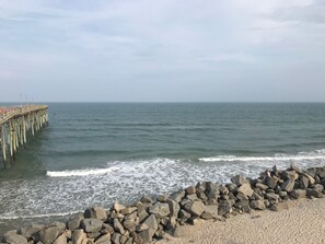 A pier extending into calm waters, a rocky shoreline, and a clear sky.