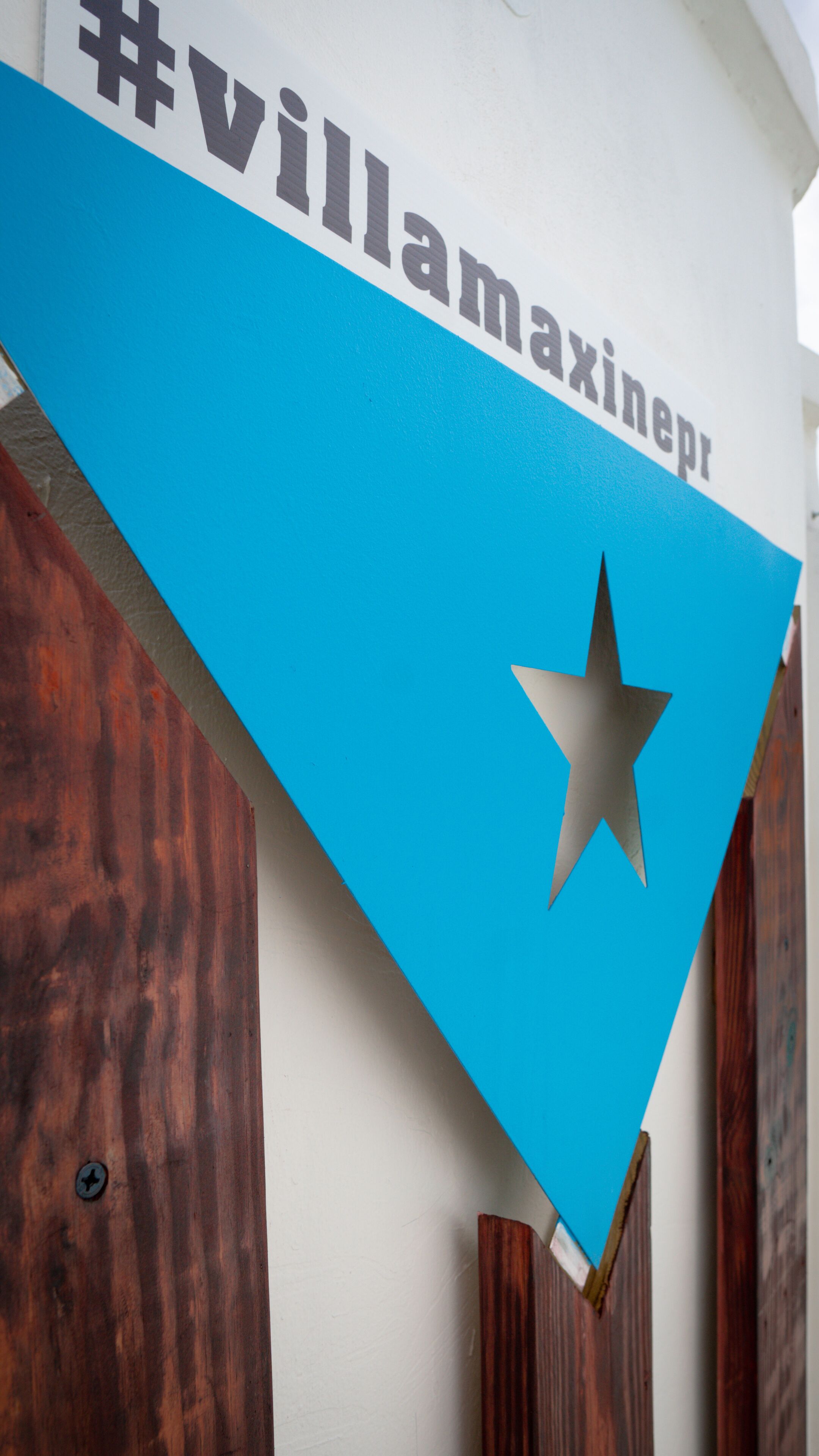 Un panneau triangulaire bleu avec une étoile blanche et le texte « #villamaxinepr » sur un mur blanc.