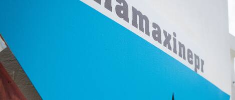 Un panneau triangulaire bleu avec une étoile blanche et le texte « #villamaxinepr » sur un mur blanc.