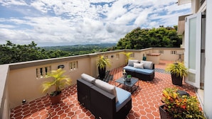 A rooftop terrace with a sofa set, a small table, and potted plants. - Villa Maxine Retreat: Mountainview Pool Near San Juan Airport (Guaynabo)