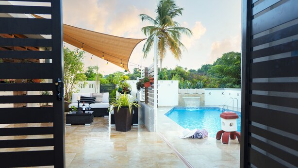 A pool area with a white fence, a palm tree, and a red and white statue. - Villa Maxine Retreat: Mountainview Pool Near San Juan Airport (Guaynabo)