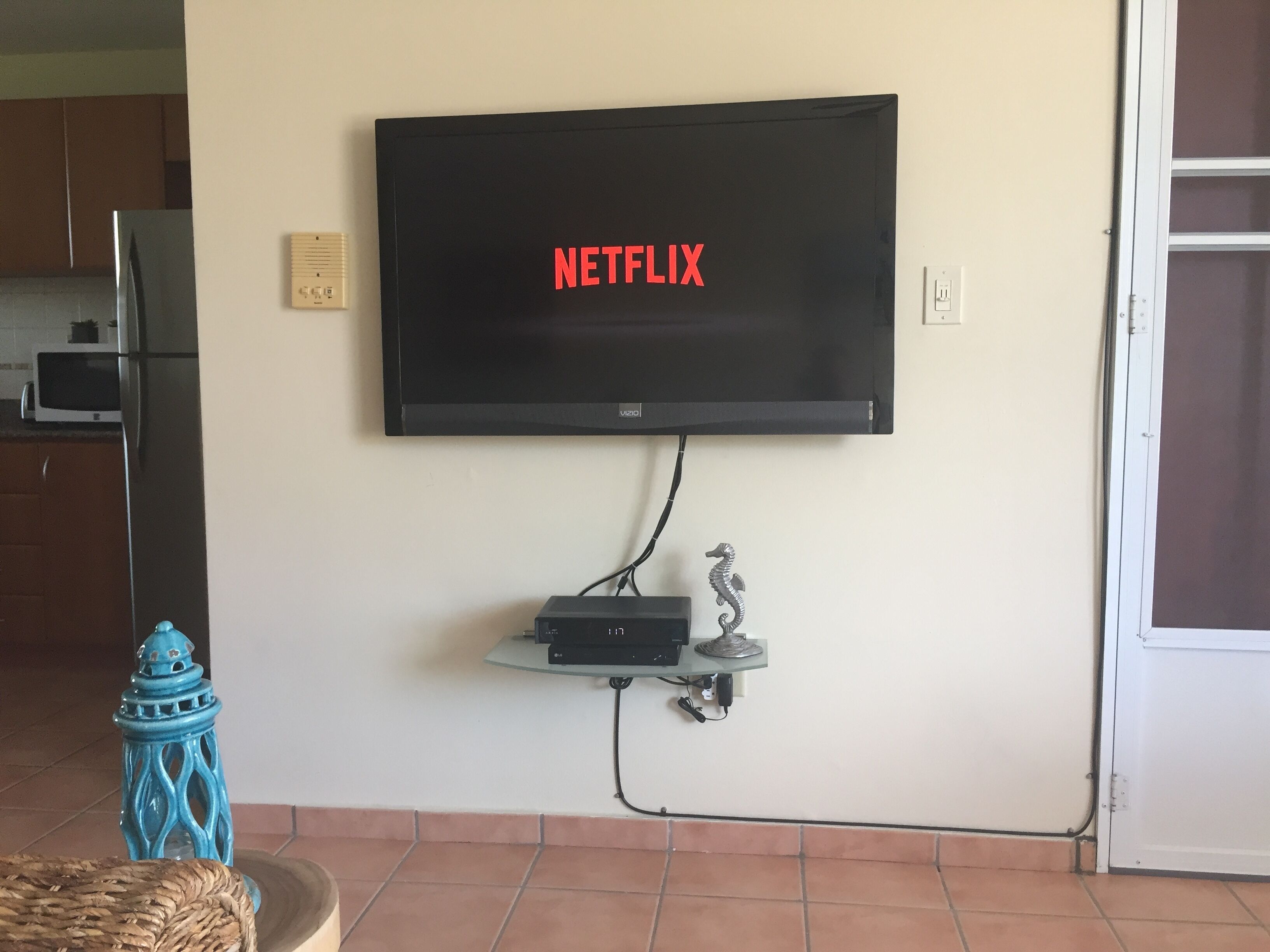 Un téléviseur à écran plat fixé au mur, orné du logo Netflix, avec une petite étagère en dessous et un hippocampe décoratif.