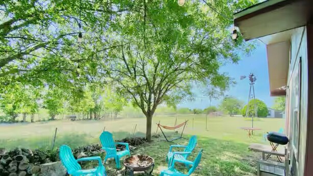 An outdoor seating area with four turquoise chairs around a fire pit, a hammock, and a view of a grassy field and trees. - The Lorena Ranchette- Goats, Firepit, Hammock (Lorena)