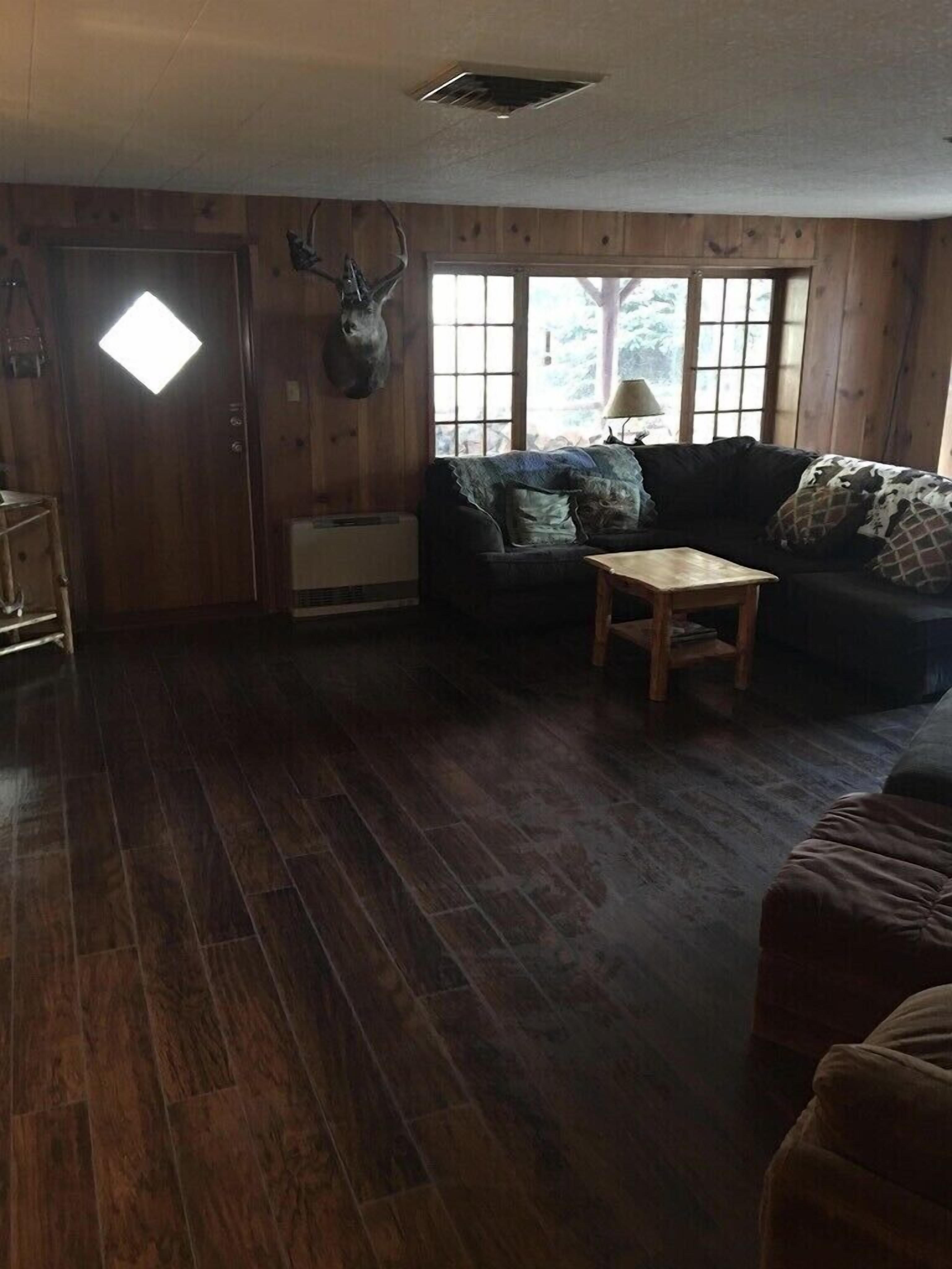 Een woonkamer met een houten vloer, een bank, een salontafel en een opgezette hertenkop aan de muur.
