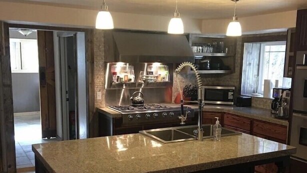 Una cocina con una isla grande, electrodomésticos de acero inoxidable e iluminación colgante.