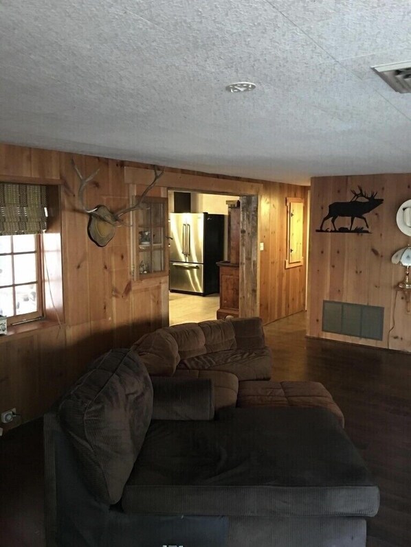 Una sala de estar con un sofá modular, paredes de madera, un adhesivo mural de venado y un respiradero en el techo.