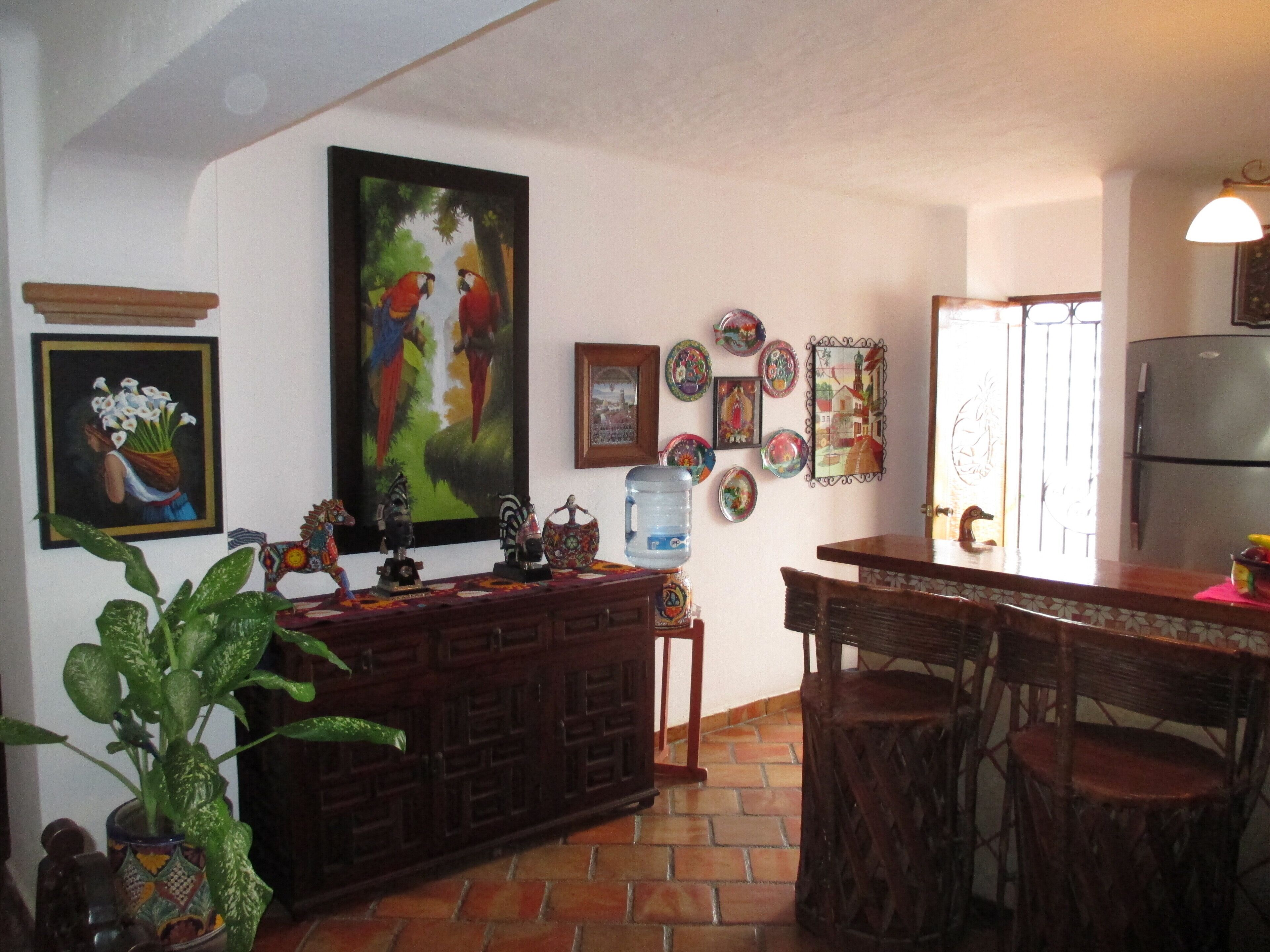 A kitchen with a tiled floor, wooden cabinets, a water dispenser, and various decorative plates on the wall.