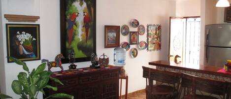 A kitchen with a tiled floor, wooden cabinets, a water dispenser, and various decorative plates on the wall.