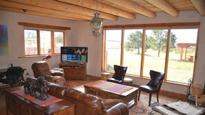 A spacious living room with leather furniture, a television, and large windows offering a view of the outdoors.