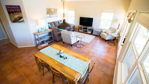 Amplia sala de estar con una mesa de comedor de madera, sofás, televisor y un ventanal grande.
