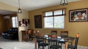 Un coin repas comprenant une table et des chaises, un canapé, un tableau et une fenêtre avec des stores.