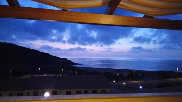 Une vue sur la mer au crépuscule, avec une montagne en arrière-plan et des lampadaires le long de la route.