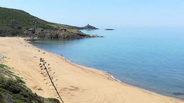 Una playa con vista despejada al mar y una colina pequeña al fondo.