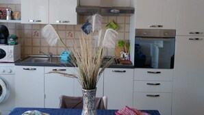Una cocina con armarios blancos, un lavamanos, una estufa y un jarrón con plantas secas.