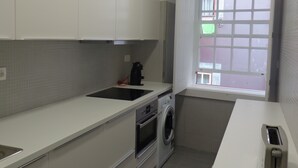 A compact kitchen with white cabinets, a built-in oven, a washing machine, and a window with a view of the street. - Apartment in the Ribeira 10 meters from the river, in the heart of the city (Porto)