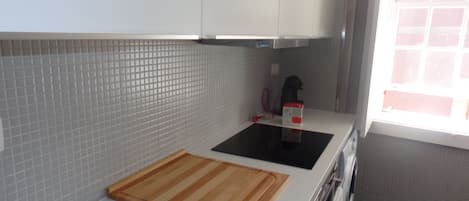 A kitchen with white cabinets, a black induction cooktop, and a wooden cutting board.