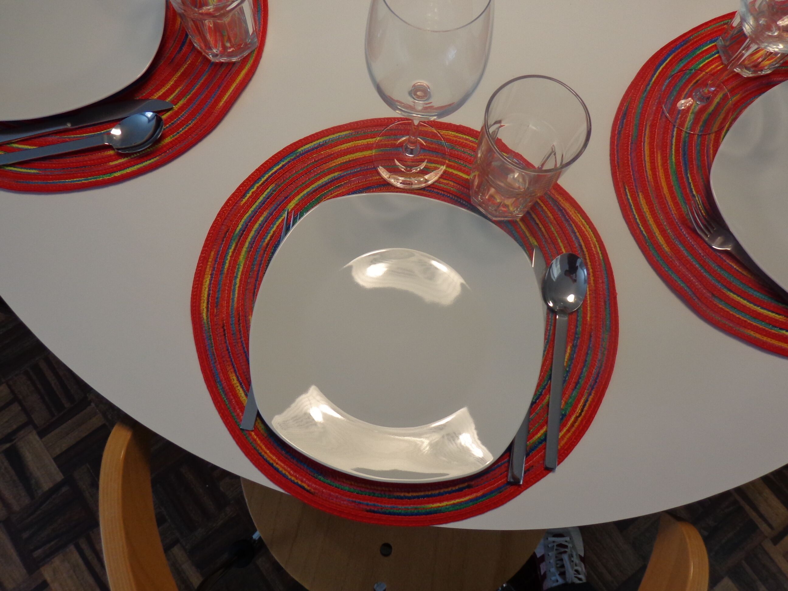 A round dining table with a white plate, a spoon, and a glass on a colorful striped placemat.