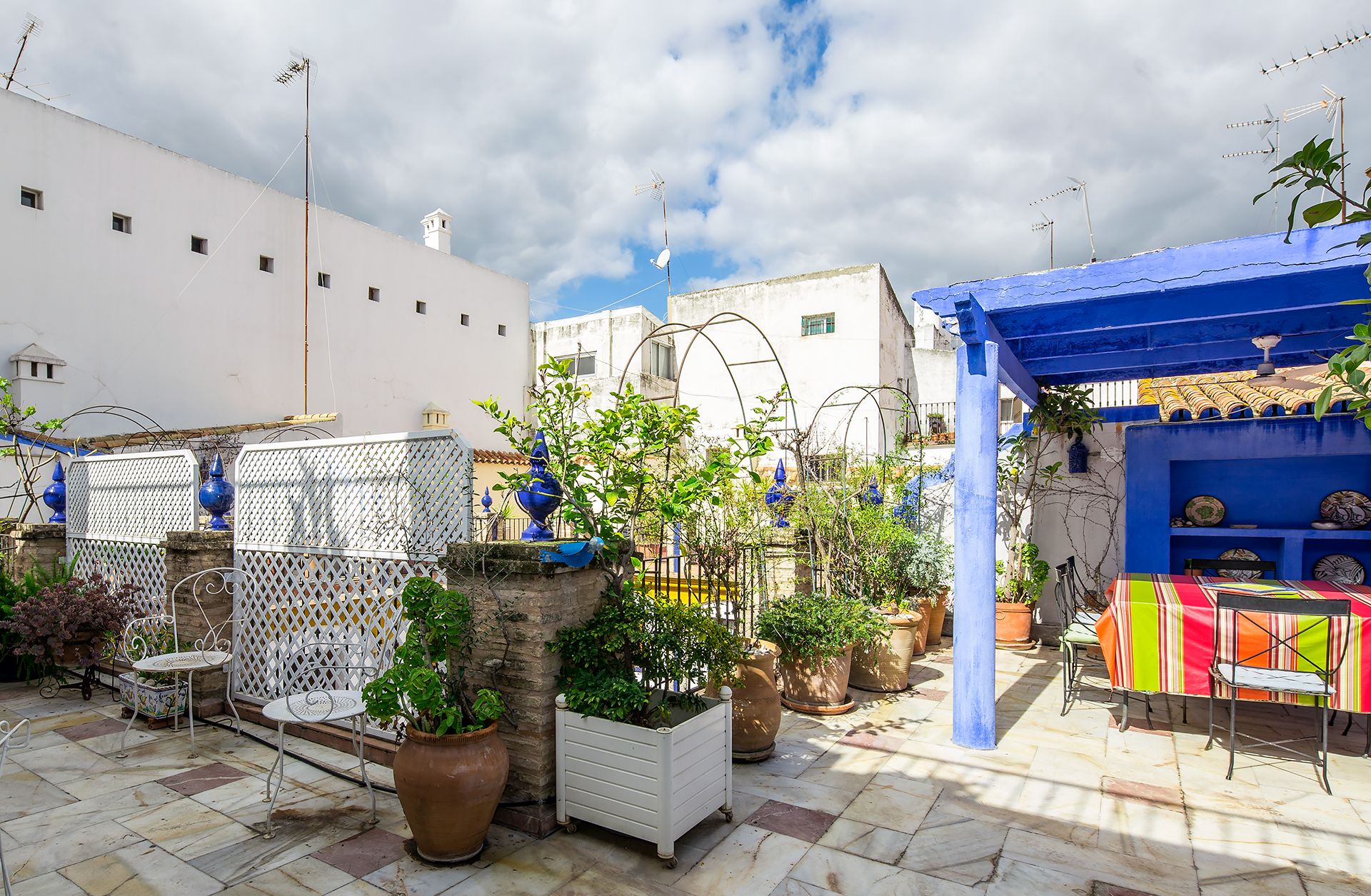 Un patio al aire libre con plantas en macetas, una mesa con sillas y un toldo azul.