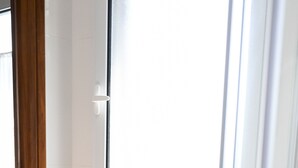 Un baño con suelo de madera, paredes blancas, un inodoro blanco y una ventana con marco blanco.