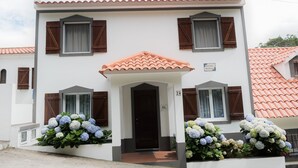 Un edificio blanco con puerta y ventanas marrones, techo de tejas y un letrero que indica un número de habitación.