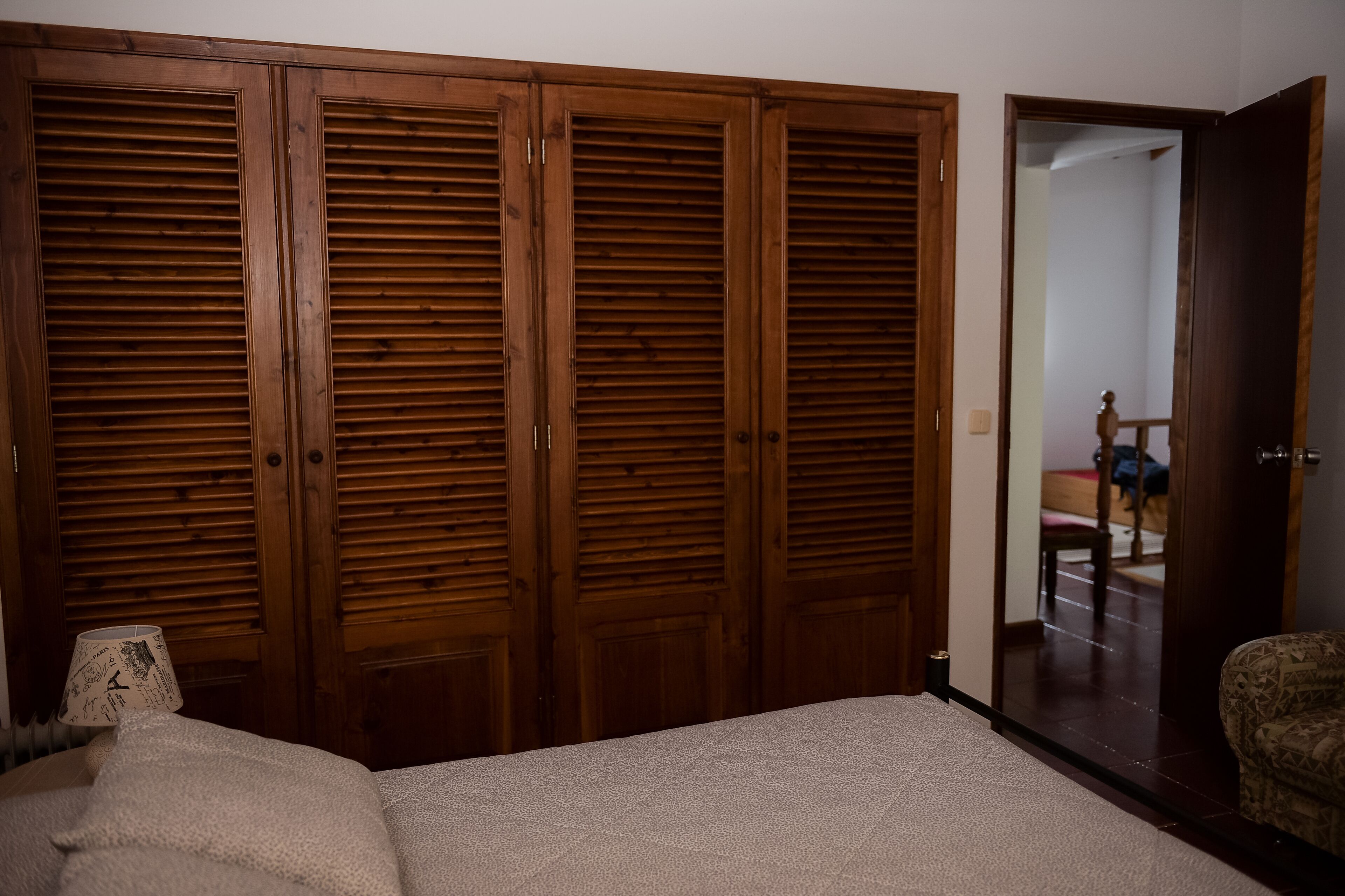 A bedroom with a large wooden wardrobe, a bed, and a chair.
