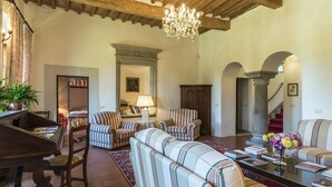 A spacious living room with a piano, striped armchairs, a sofa, and a chandelier. - Villa Palazzaccio 26, Emma Villas (Arezzo)