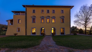 A two-story building with a symmetrical facade, multiple windows with curtains, and a gravel pathway leading to the entrance. - Villa Palazzaccio 26, Emma Villas (Arezzo)