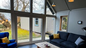 A modern living room with a blue armchair, a dark blue sofa, and a wooden coffee table. - Traditional Loch Side Croft Cottage And Garden With Contemporary Extension (Acharacle)