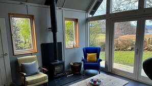 A cozy living room with a fireplace, comfortable seating, and large windows offering a view of the outdoors. - Traditional Loch Side Croft Cottage And Garden With Contemporary Extension (Acharacle)