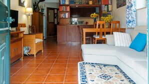 A cozy living room with a sofa, a coffee table, and a bookshelf filled with books. There is a dining area with chairs and a table, and a kitchen in the background. - House in quiet area of ​​housing. But close to the center. (Sintra)