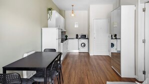 A modern kitchen with white appliances, a dining table with chairs, and a hanging light fixture. - Apartamento D'alegria 1 by Amber Star Rent (Porto)