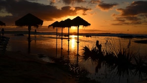 A sunset over a calm body of water with thatched-roof structures.