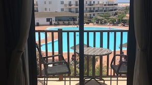 A balcony with a view of a swimming pool, lounge chairs, and a table.