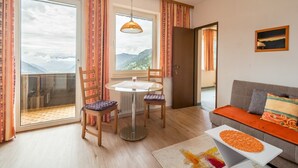 Ein modernes Wohnzimmer mit einer Couch, einem Esstisch und Stühlen. Große Fenster bieten Blick auf Berge.