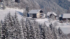Eine verschneite Berglandschaft mit mehreren Holzbauten, darunter eine markante, zweistöckige Lodge mit einem Balkon.
