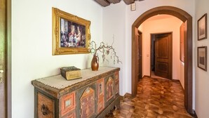 Ein Flur mit Holzboden, einem alten Schrank, einem gerahmten Gemälde und einer Vase mit Zweigen.