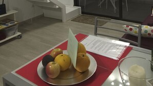 Een moderne kamer met balkon en uitzicht op zee bij zonsondergang, een eettafel met fruit, en een trap.