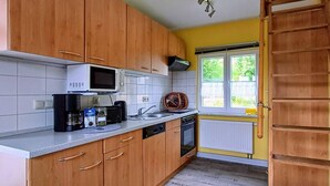 A compact kitchen with wooden cabinets, a microwave, a coffee maker, and a window with a view of greenery. - Vacation hut on the Goethe Trail with a view, close to the Rennsteig, UNESCO biosphere reserve (Ilmenau)