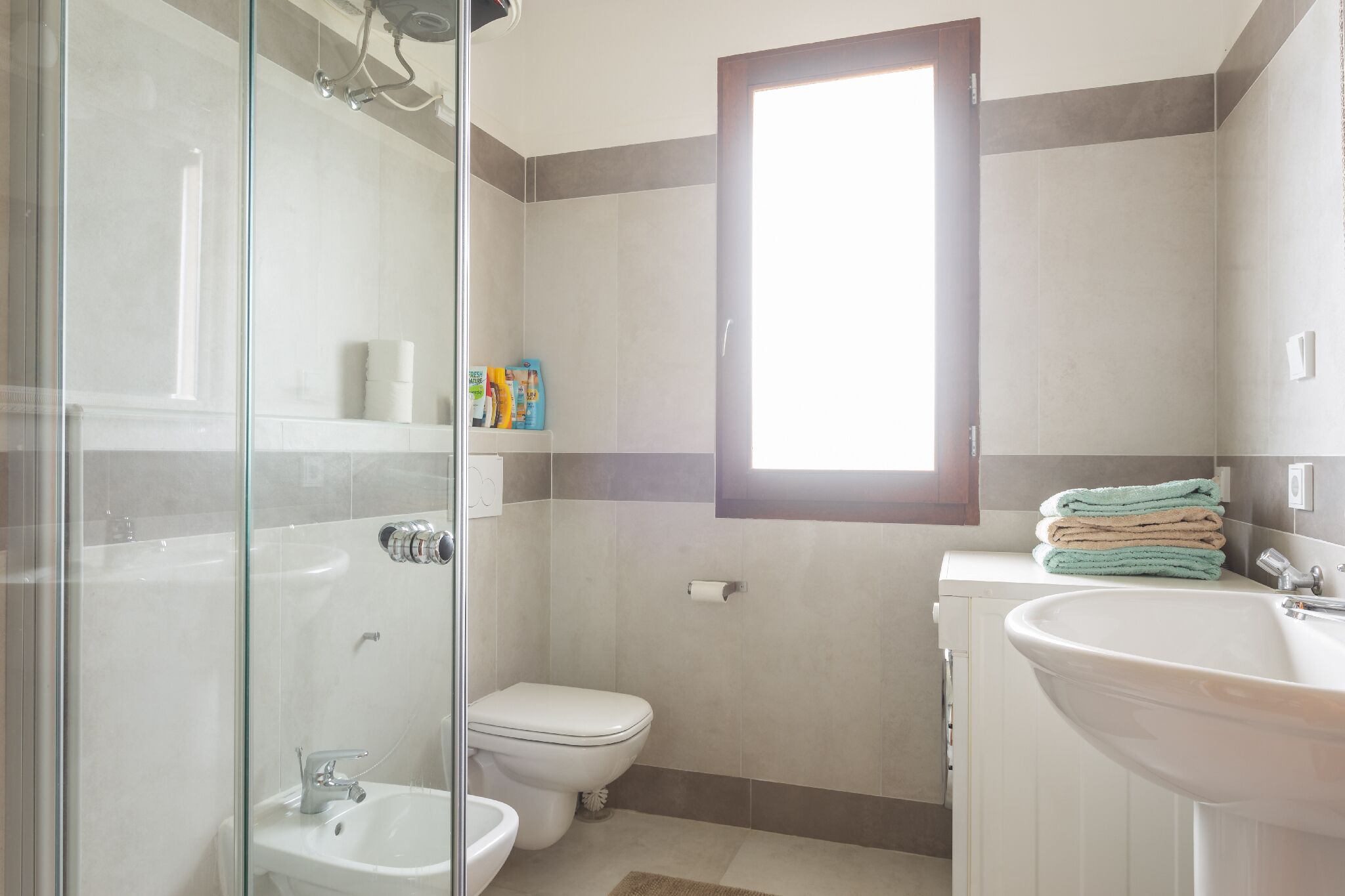 Une salle de bain avec une douche à parois de verre, des toilettes, un lavabo et une fenêtre.