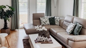 Un salon moderne avec un canapé d’angle beige, une table basse blanche et une grande plante en pot.