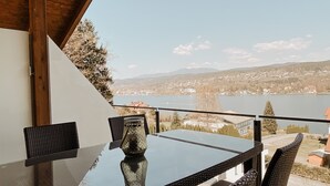 Une table à plateau en verre, des chaises en osier, un vase et, en arrière-plan, une vue sur un lac et une ville.