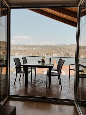 Ein Essbereich mit Tisch und Stühlen, einer Vase und Blick auf einen See sowie Gebäude in der Ferne.