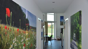 Un couloir orné de grandes peintures florales, une table avec des chaises et une vue sur l’extérieur grâce à une porte vitrée.