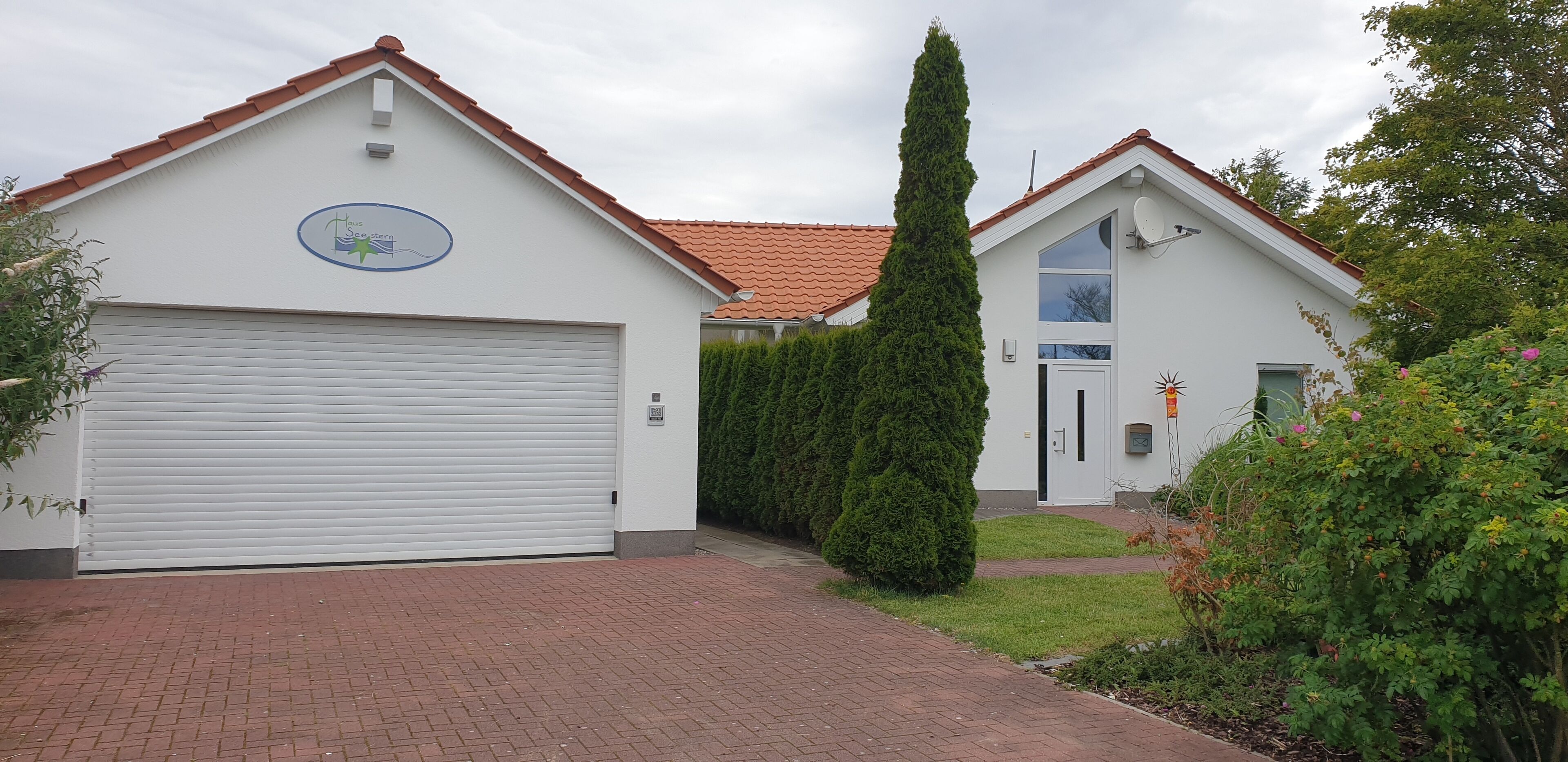 Un bâtiment à deux étages, doté d’un garage et d’une porte, entouré de verdure et bordé d’un chemin en briques.