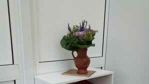 A white shelf with a brown vase containing a floral arrangement, red and green folded blankets, and a small metal object on a white table.