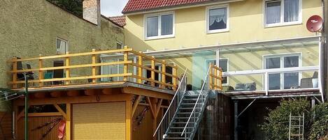 Une maison à deux étages avec un toit recouvert de tuiles rouges, une terrasse en bois et un garage.
