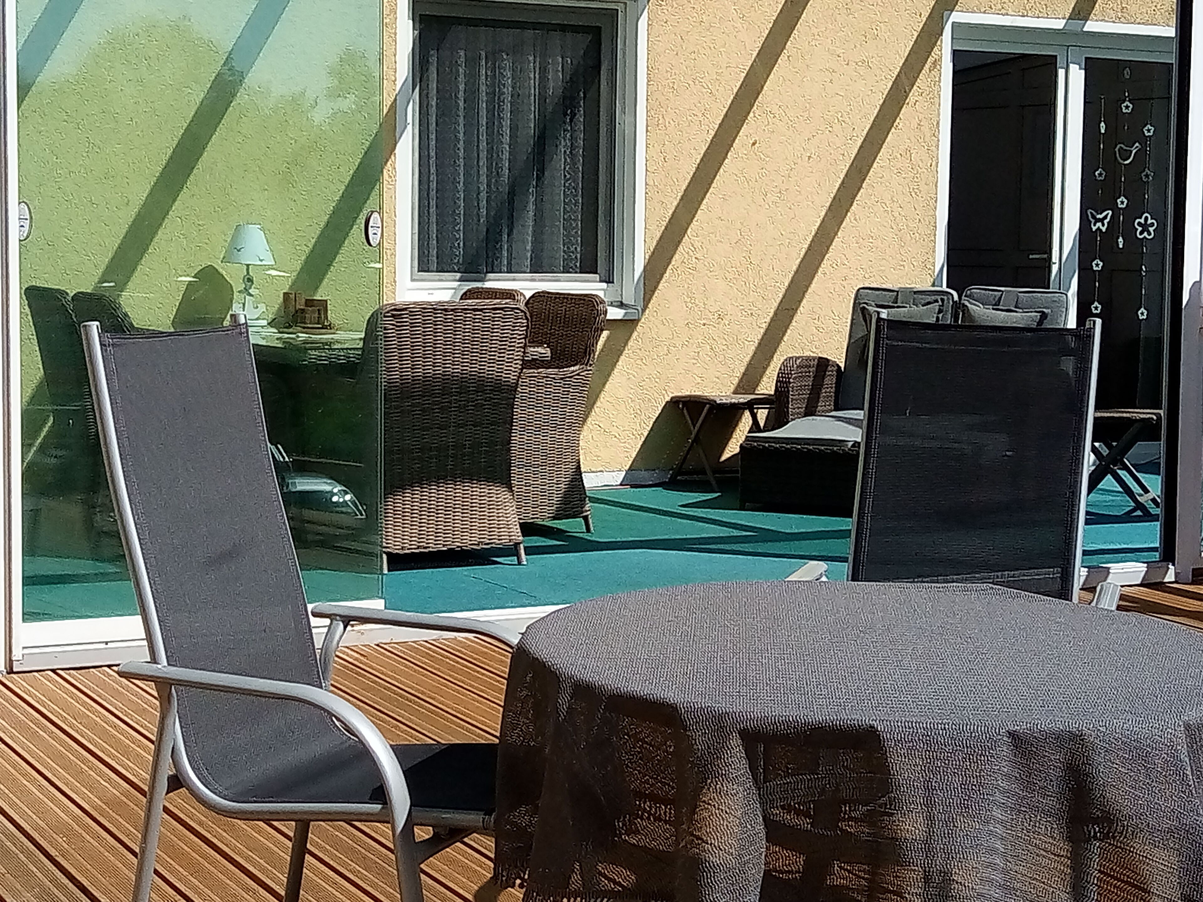 Ein sonniger Außenbereich mit Korbmöbeln, einem Tisch und einer Glastür, die auf einen Balkon führt.