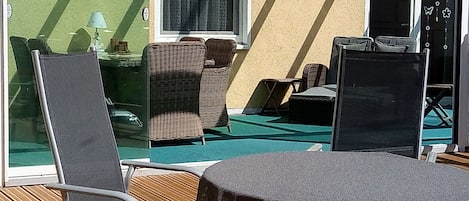 Ein sonniger Außenbereich mit Korbmöbeln, einem Tisch und einer Glastür, die auf einen Balkon führt.