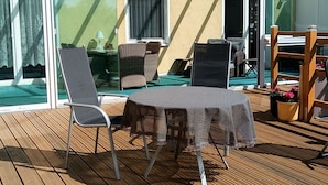 A sunlit outdoor area with a table and chairs, a sliding glass door, and a wicker chair.